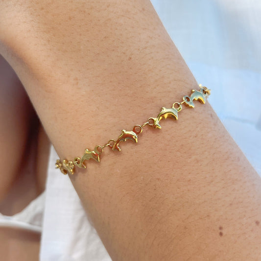 A person's wrist wearing a golden bracelet with mini dolphin charms.