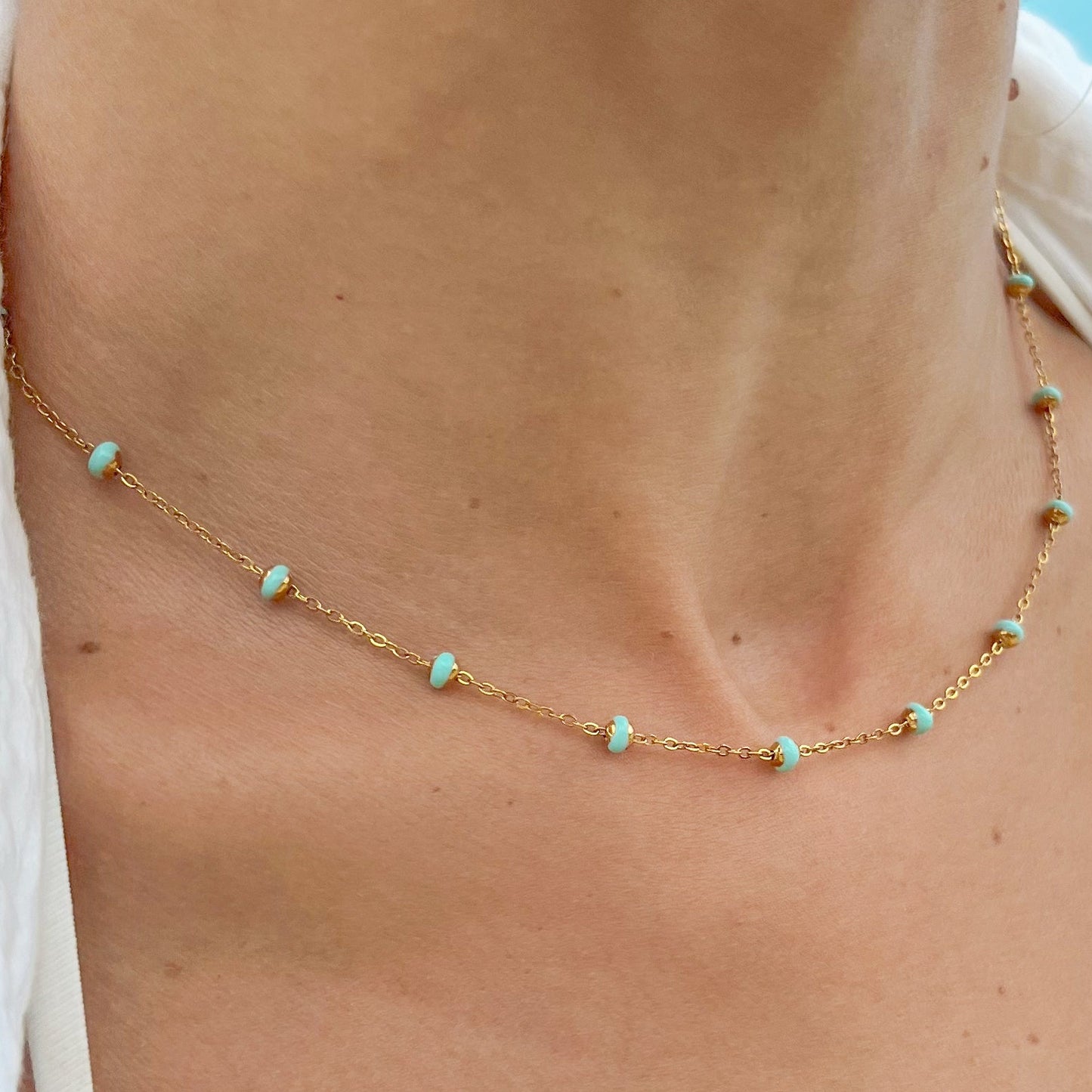 A close-up image of a person wearing a gold-colored necklace with ocean-blue beads.