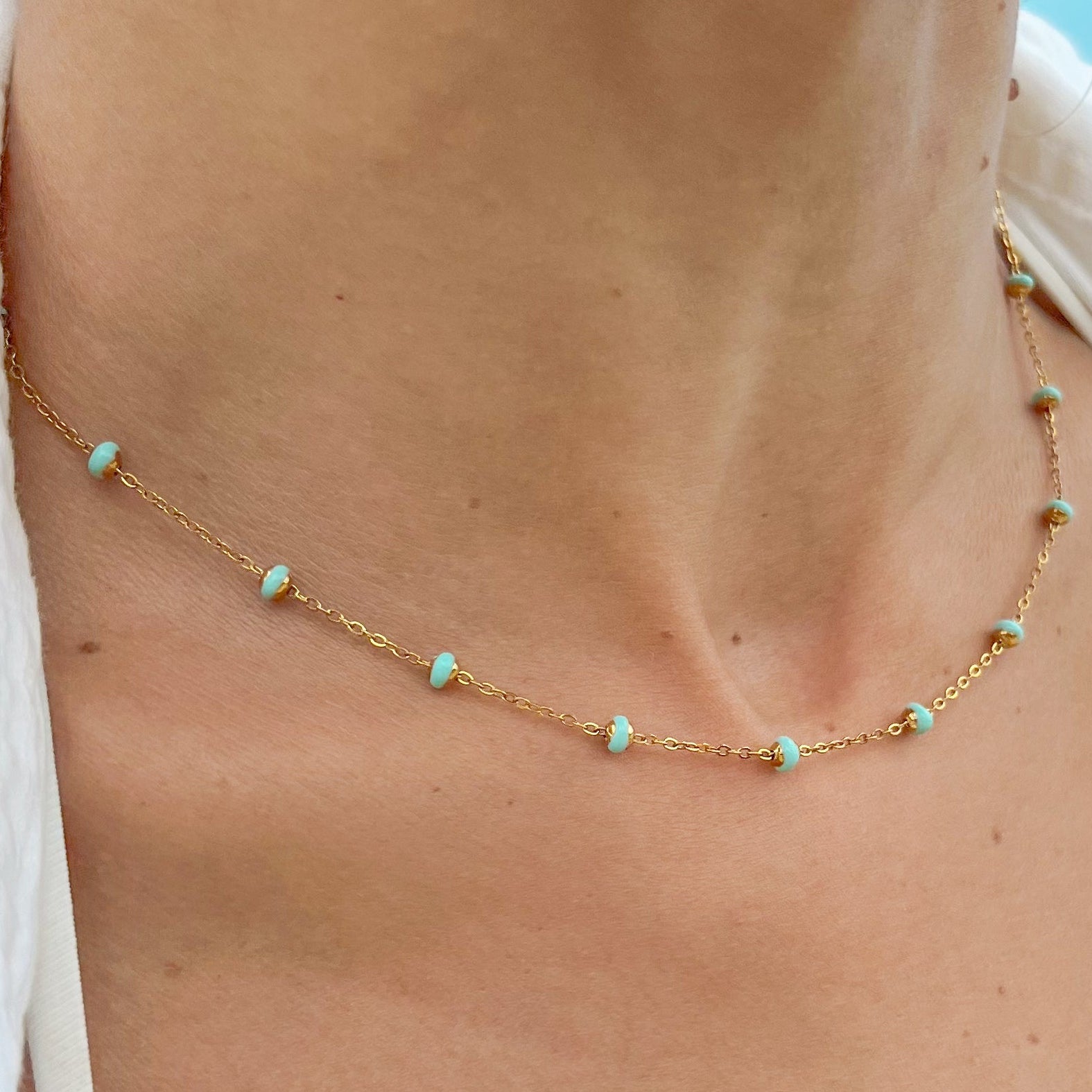 A close-up image of a person wearing a gold-colored necklace with ocean-blue beads.